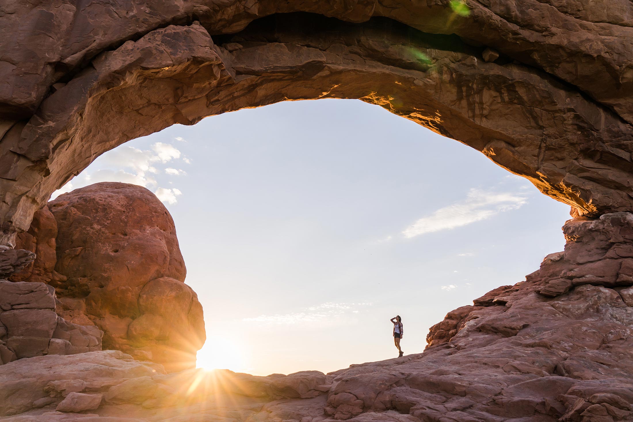 View of hiker under red rock arch in Moab, UT.